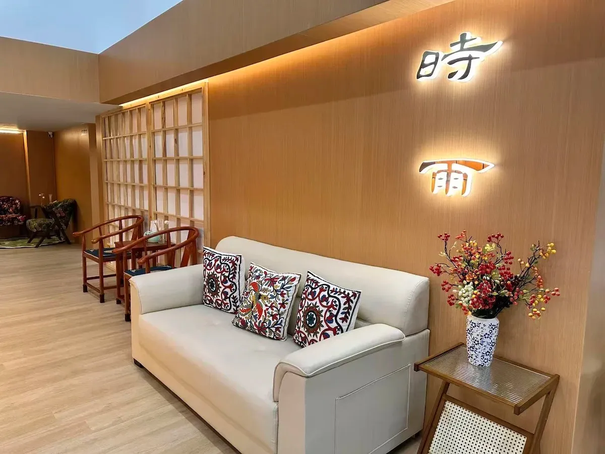 接待大厅,暖色木质墙面上有发光的「时雨」字样,白色沙发与中式木椅